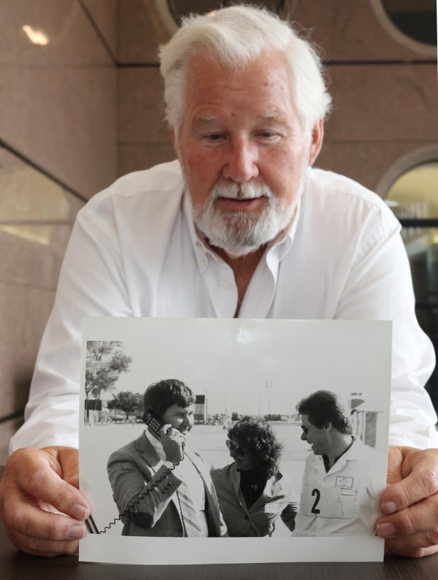 In his Oakbrook Terrace office on Oct. 12, 2023, David Meilahn holds a 1983 photo of himself making the first commercial cellphone call alongside his wife, Gail Meilahn, and technician Jeff Benuzzi. (Stacey Wescott/Chicago Tribune)