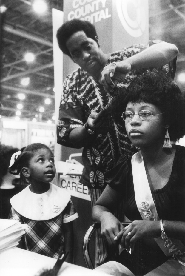 Jeanine Arnold, 4, of 7817 S. Marshfield, watches Maurice Johnson of 757 East 87th Street, set the hair of Janice Anderson of 6045 S. King Drive at the Black Expo on Oct. 2, 1971. (Don Casper/Chicago Tribune)