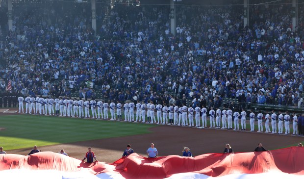 The Chicago Cubs stand for the national anthem before Game...
