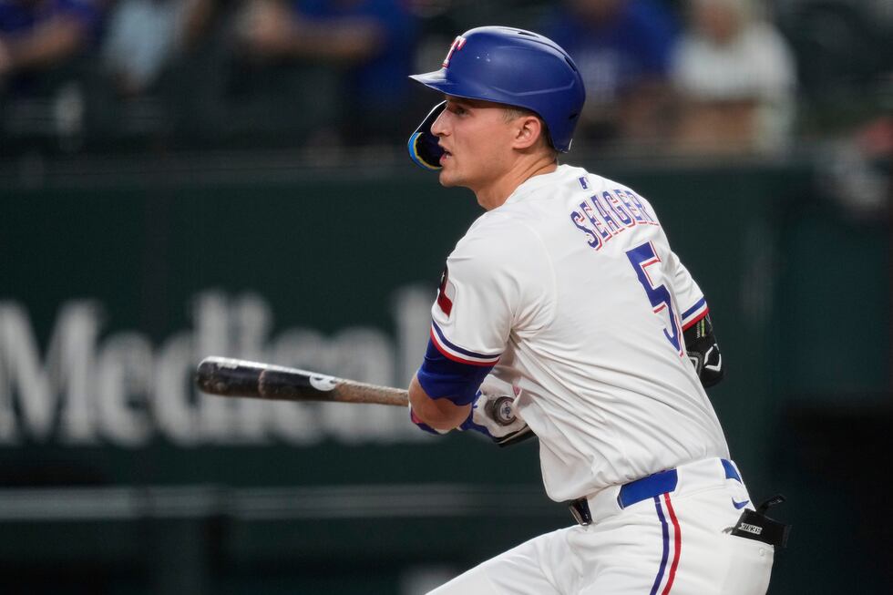 Texas Rangers' Corey Seager follows through on a single in the first inning of a baseball game...