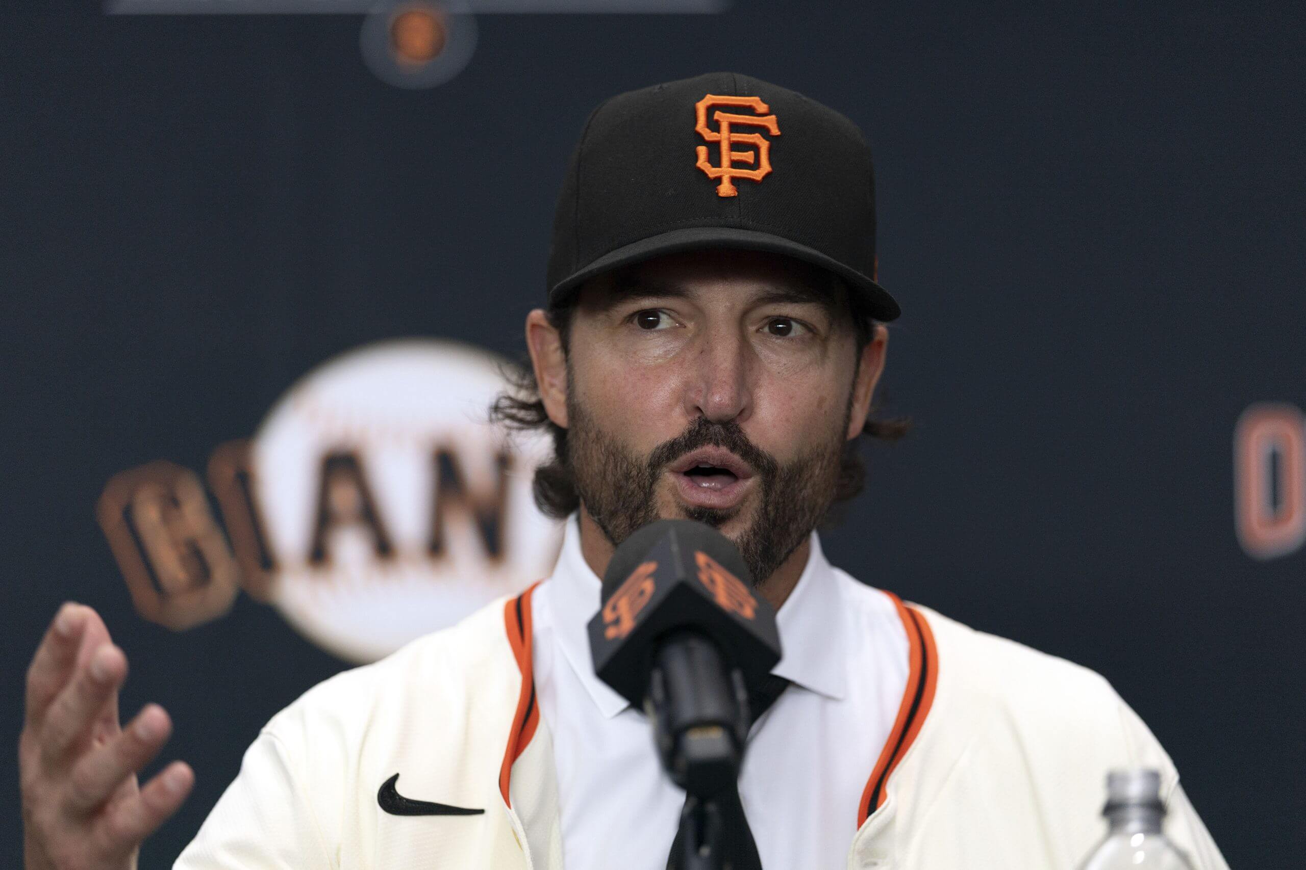 Tony Vitello speaks while wearing a Giants cap and jersey.