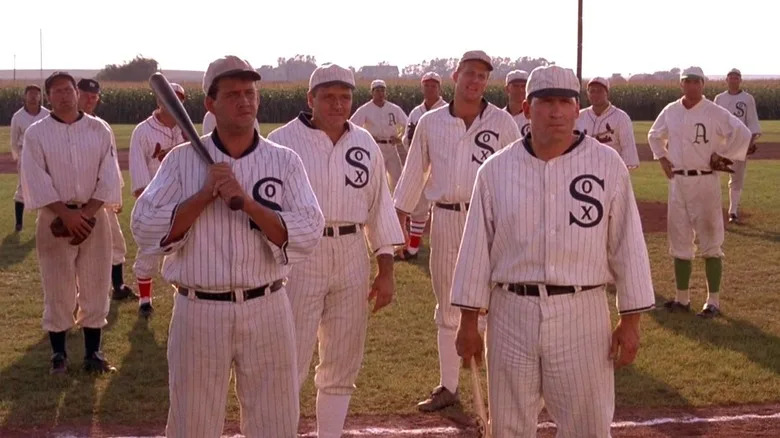 Eddie Cicotte, Buck Weaver, and Chick Gandil stand in front of other baseball players on the baseball field in Field of Dreams