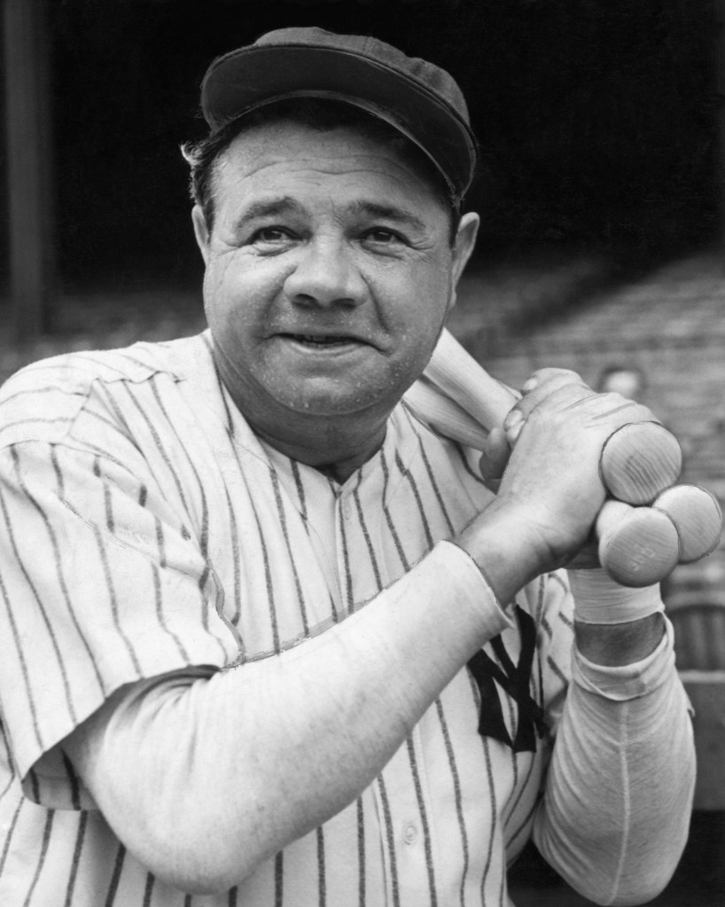 Babe Ruth holding warm-up bats in his baseball uniform.