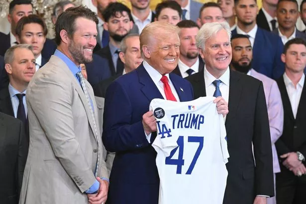 TOPSHOT - US President Donald Trump holds up a jersey alongside pitcher Clayton Kershaw (L) and team owner Mark Walter (R) during an event honoring the 2024 World Series champions Los Angeles Dodgers in the East Room of the White House in Washington, DC, on April 7, 2025. (Photo by SAUL LOEB / AFP) (Photo by SAUL LOEB/AFP via Getty Images)          