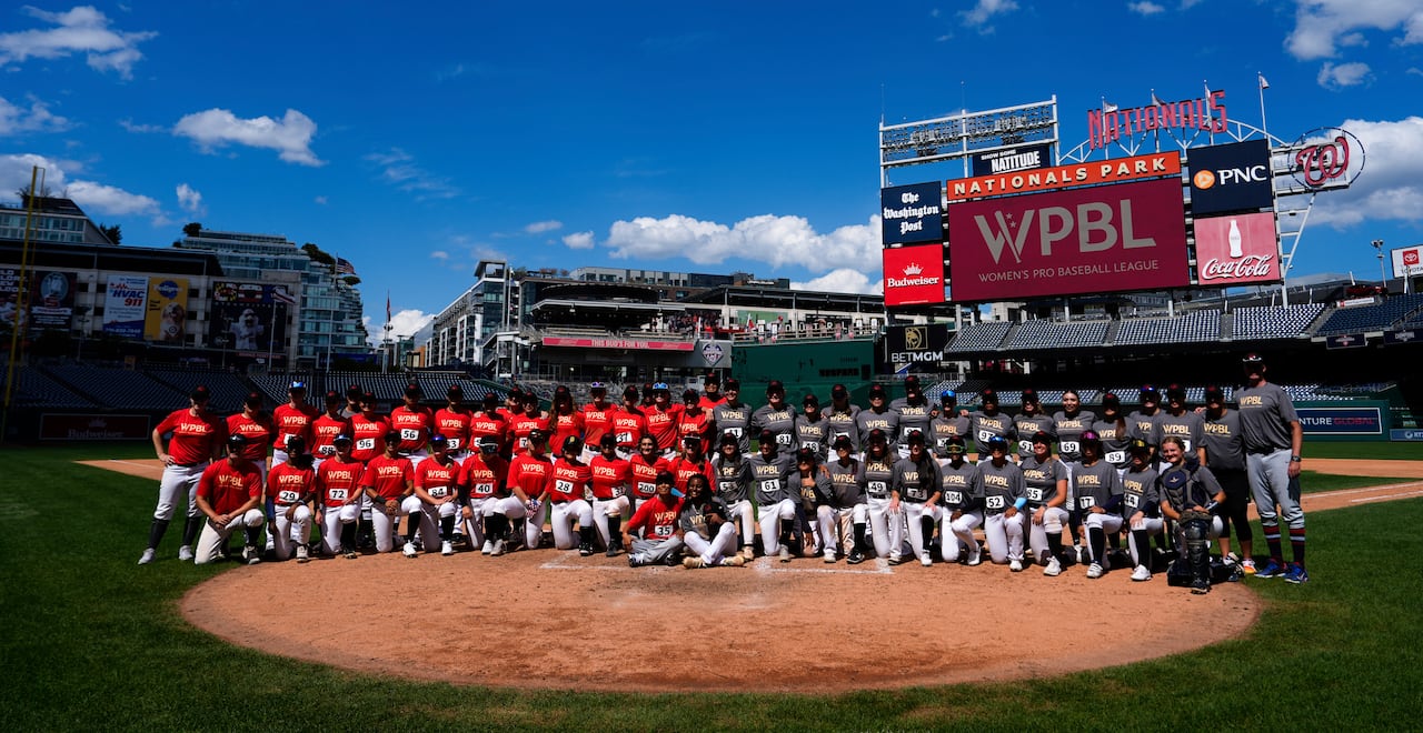 A group of baseball players pose for a picture on a sunny day in a stadium.