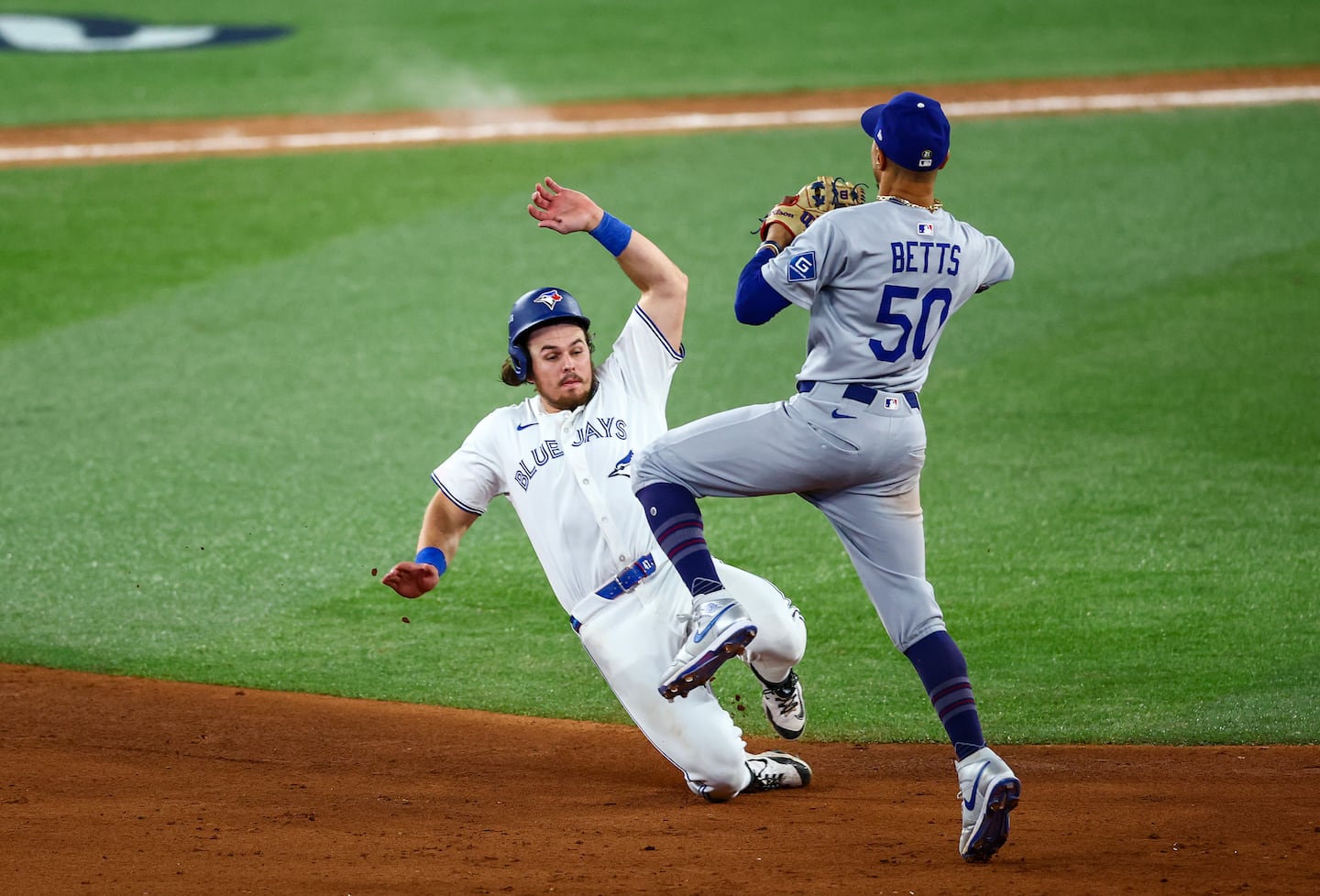 Shortstop Mookie Betts #50 of the Los Angeles Dodgers turns a double play as third baseman Addison Barger #47 of the Toronto Blue Jays slides into second base to end the game in the 11th inning of the 2025 World Series.