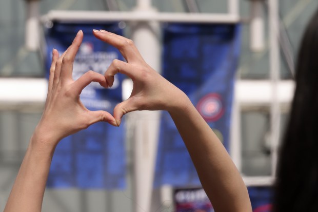 A baseball fan makes a heart shape symbol while posing...
