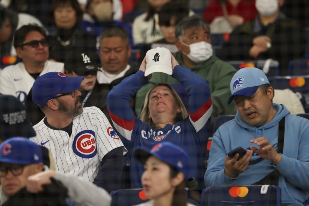 A Cubs fan adjusts her cap after taking her seat...