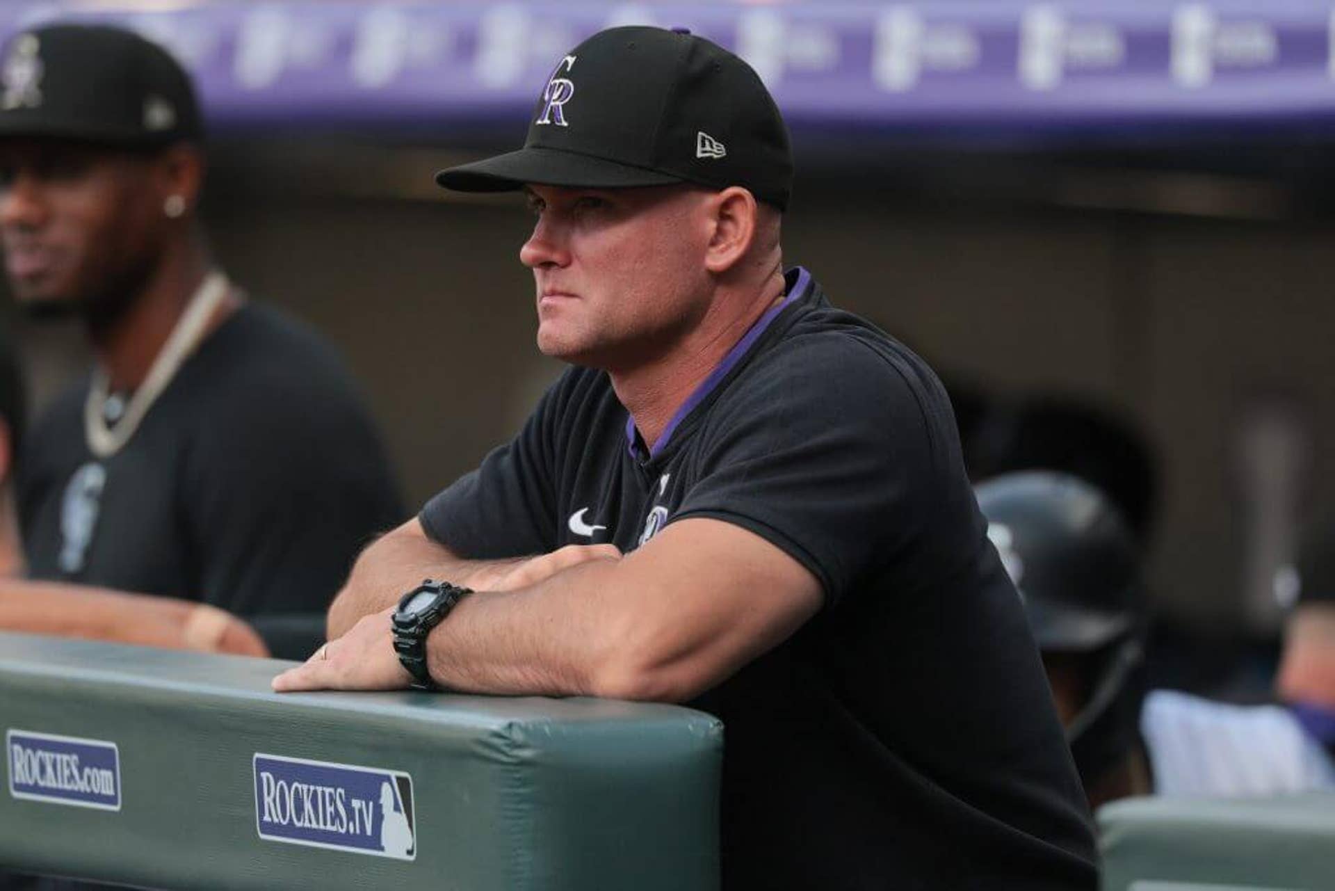 Colorado Rockies manager Warren Schaeffer rests his elbows on a ledge and looks out from the dugout during an MLB game.