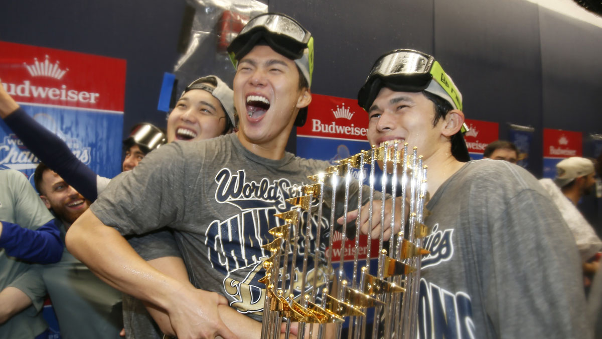 Los Angeles Dodgers two-way player Shohei Ohtani (17) and pitcher Yoshinobu Yamamoto (18) and pitcher Roki Sasaki (11) celebrate with the Commissioner's Trophy in the clubhouse after defeating the Toronto Blue Jays in the 2025 MLB World Series at Rogers Centre. 