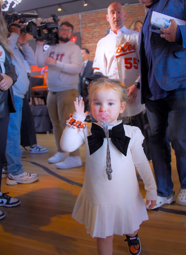 Gnawing on her binkie, Genevieve Elizabeth Albernaz waves while walking in front of her father Craig Albernaz, newly hired as manager of the Baltimore Orioles following a press conference at Oriole Park at Camden Yards. (Karl Merton Ferron/Staff)