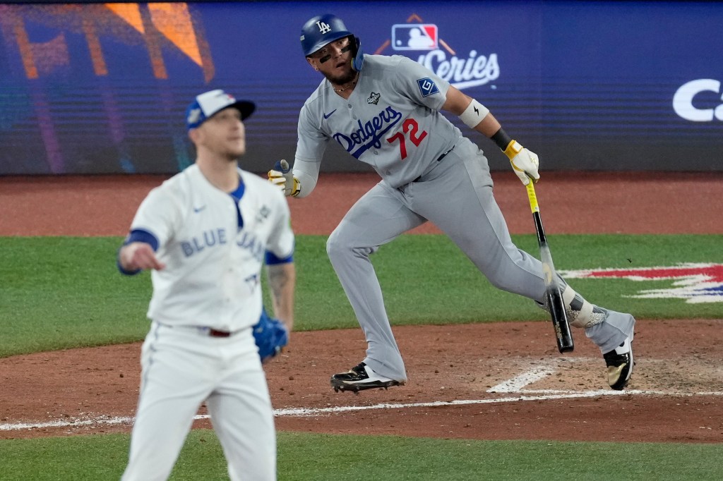 Los Angeles Dodgers' Miguel Rojas watches his home run take flight, while Toronto Blue Jays' pitcher Jeff Hoffman watches in the background.