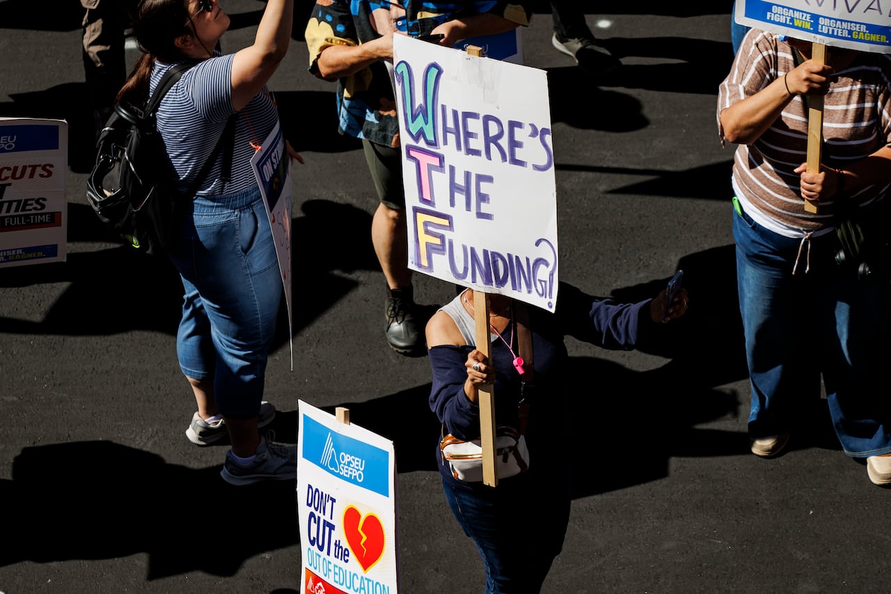 Picketers striking outside, with posters that read: Where's the funding? and Don't cut the heart out of education.