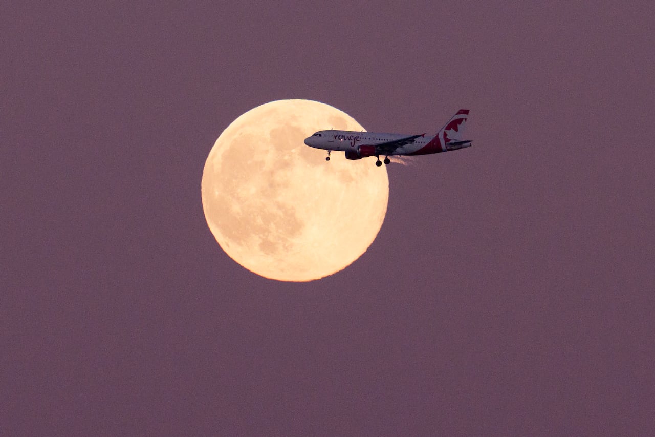 A plane flying past a full moon.