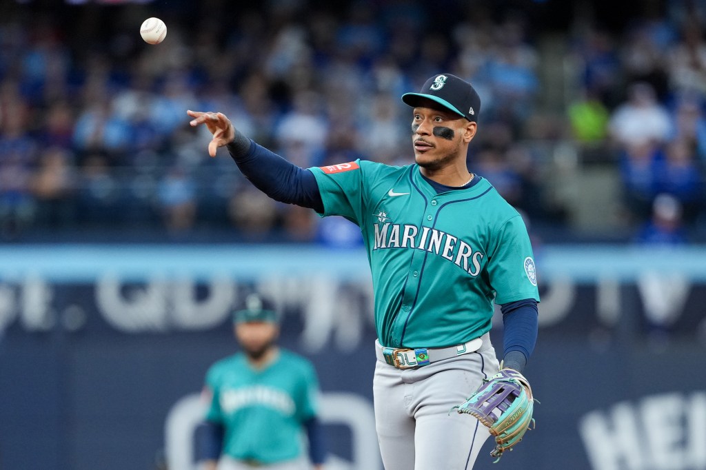 A Seattle Mariners player in a teal jersey with eye black throwing a baseball.
