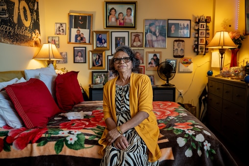 Nelly Orellana, 70, poses for a portrait in her apartment at the Victory Tower affordable senior living facility in Takoma Park, Md. on Wednesday, Nov. 5, 2025. Behind her, photos of her family plaster the wall.
