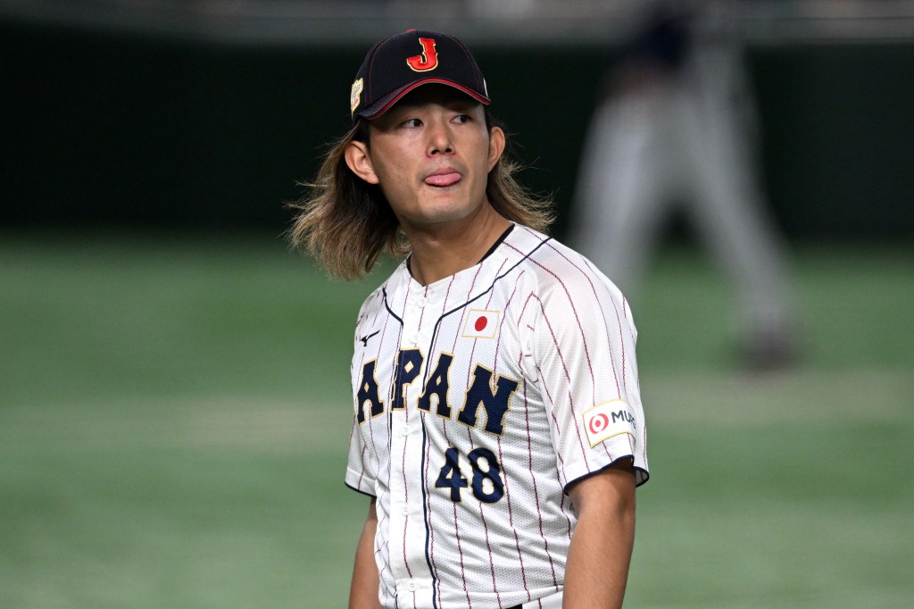 Japanese baseball player Kenta Maeda in a white pinstriped jersey with "JAPAN" and "48" in dark blue, wearing a dark blue cap with a red "J", sticking out his tongue.