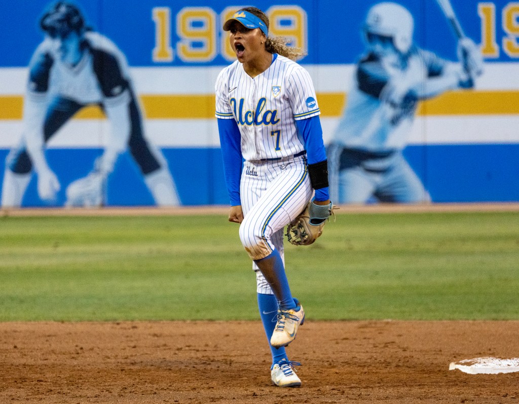 UCLA softball player in blue and white uniform with number 7 shouting with excitement on the field.