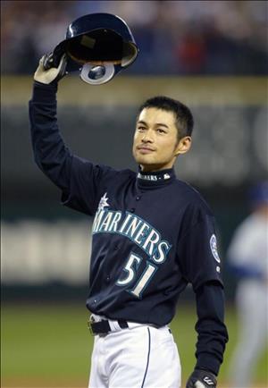 A young asian man in a blue baseball uniform waves his batting helmet in the air. His jersey says mariners above the number fifty one.
