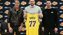 Slovenian basketball player Luka Doncic (C) holds up a jersey as he stands alongside Los Angeles Lakers head coach JJ Redick (R) and Los Angeles Lakers general manager Rob Pelinka  during a press conference introducing Doncic as the newest member of the Los Angeles Lakers, at the UCLA Health Training Center, in El Segundo, California on February 4, 2025. Slovenian star Luka Doncic said February 2, 2025 he thought he'd spend his entire NBA career in Dallas, thanking fans in Texas for making it feel like home a day after the Mavericks abruptly traded him to the Los Angeles Lakers. (Photo by Patrick T. Fallon / AFP) (Photo by PATRICK T. FALLON/AFP via Getty Images)