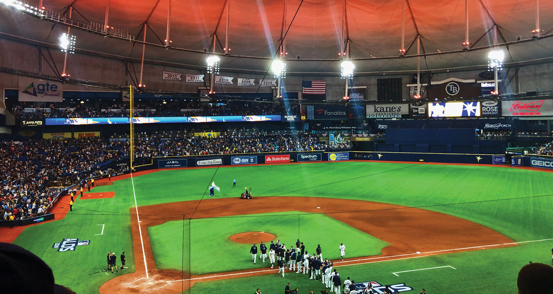 The inside of Tropicana Field, home of the baseball team the Tampa Bay Rays. Lit with orange ceiling and green grass after a game