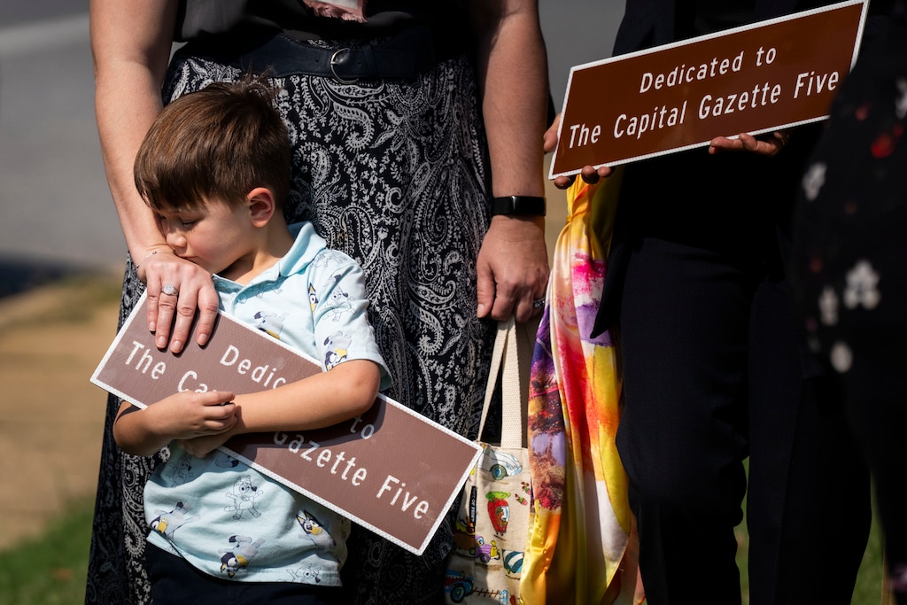 Orion Larca hugs a smaller version of a highway marker dedicated to his grandmother Wendi Winters, while his mother Winters Larca, Wendi's daughter, stands behind him on September 22, 2025. "The Capital Gazette Five" are victims of a deadly shooting on the The Capital Gazette in 2018. Winters was a photojournalist who was killed saving the lives of her colleagues.