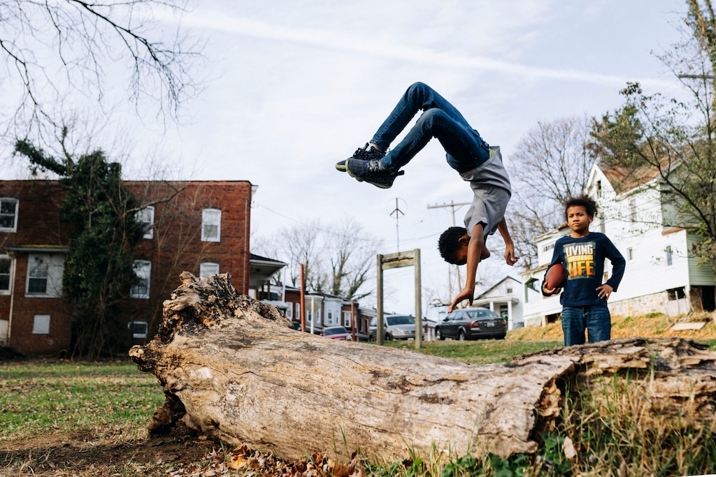 Dwayne Watkins flips off a log in the Peace Park, while Noah Duncan watches in the Collins Streamside Community of Southwest Baltimore, MD on Thursday, Dec. 5, 2024.