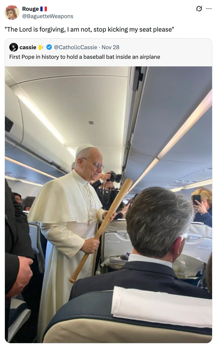 A person dressed in a white religious robe holds a baseball bat while standing in an airplane aisle, engaging with passengers