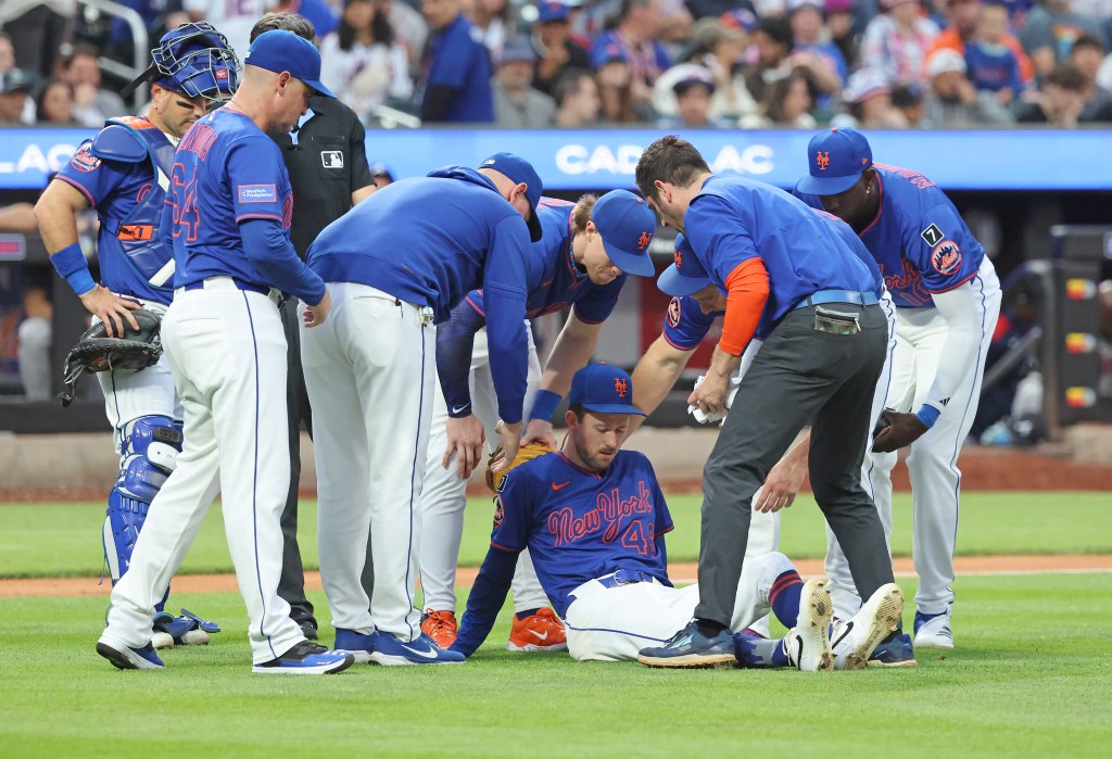 Griffin Canning #46 of the New York Mets lays on the floor as trainers check on him after injuring himself during the third inning.