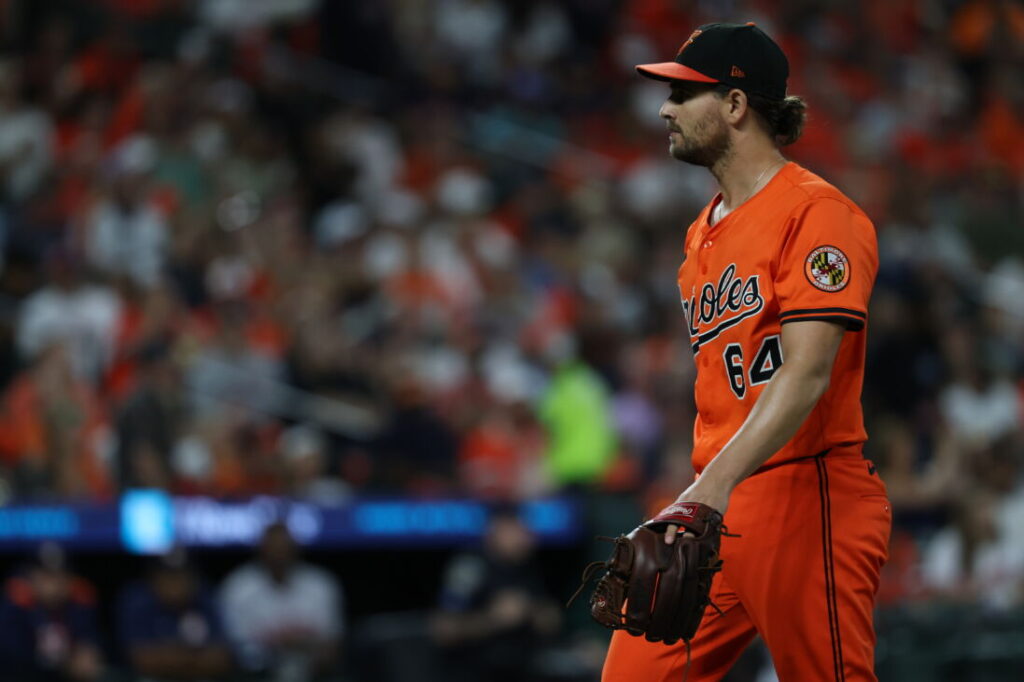 A man wearing an orange baseball uniform and a baseball glove.