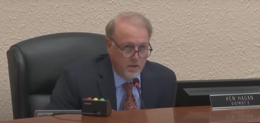 Man with glasses, goatee and sitting in a black swivel chair speaking into a microphone. 