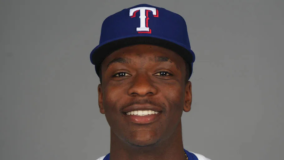 A baseball player smiling while wearing a blue Texas Rangers ball cap