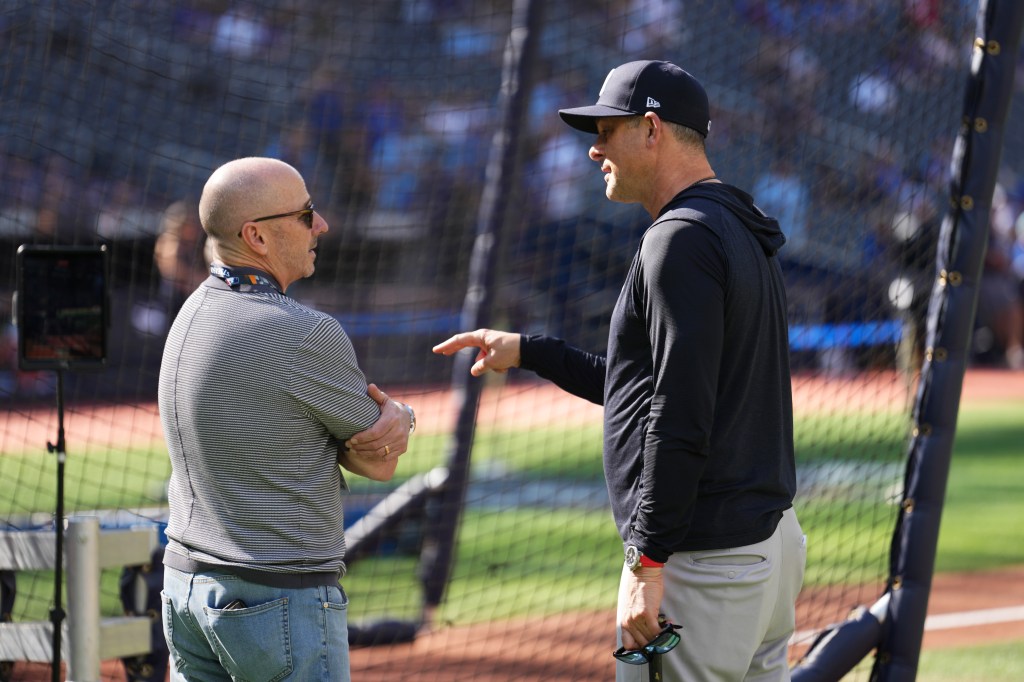 Two men, one in a baseball cap and the other with sunglasses, talking on a baseball field.