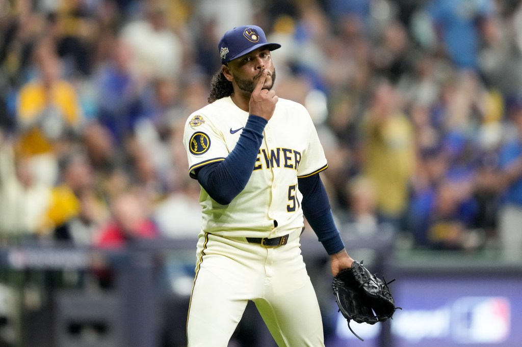 Milwaukee Brewers pitcher Freddy Peralta looks on with his finger to his mouth, holding a baseball glove.