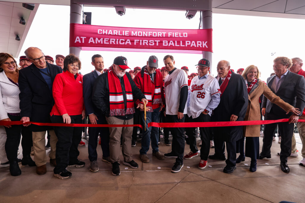 Group cuts a red ribbon beneath a “Charlie Monfort Field at America First Ballpark” banner.