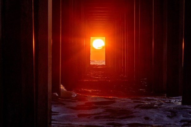 The sun sets between the pilings of the Ellen Browning Scripps Memorial Pier on Thursday, Aug. 7, 2025 in San Diego, CA. This rare phenomenon known to locals as "Scrippshenge" occurs twice a year, in May and August. (Meg McLaughlin / The San Diego Union-Tribune)