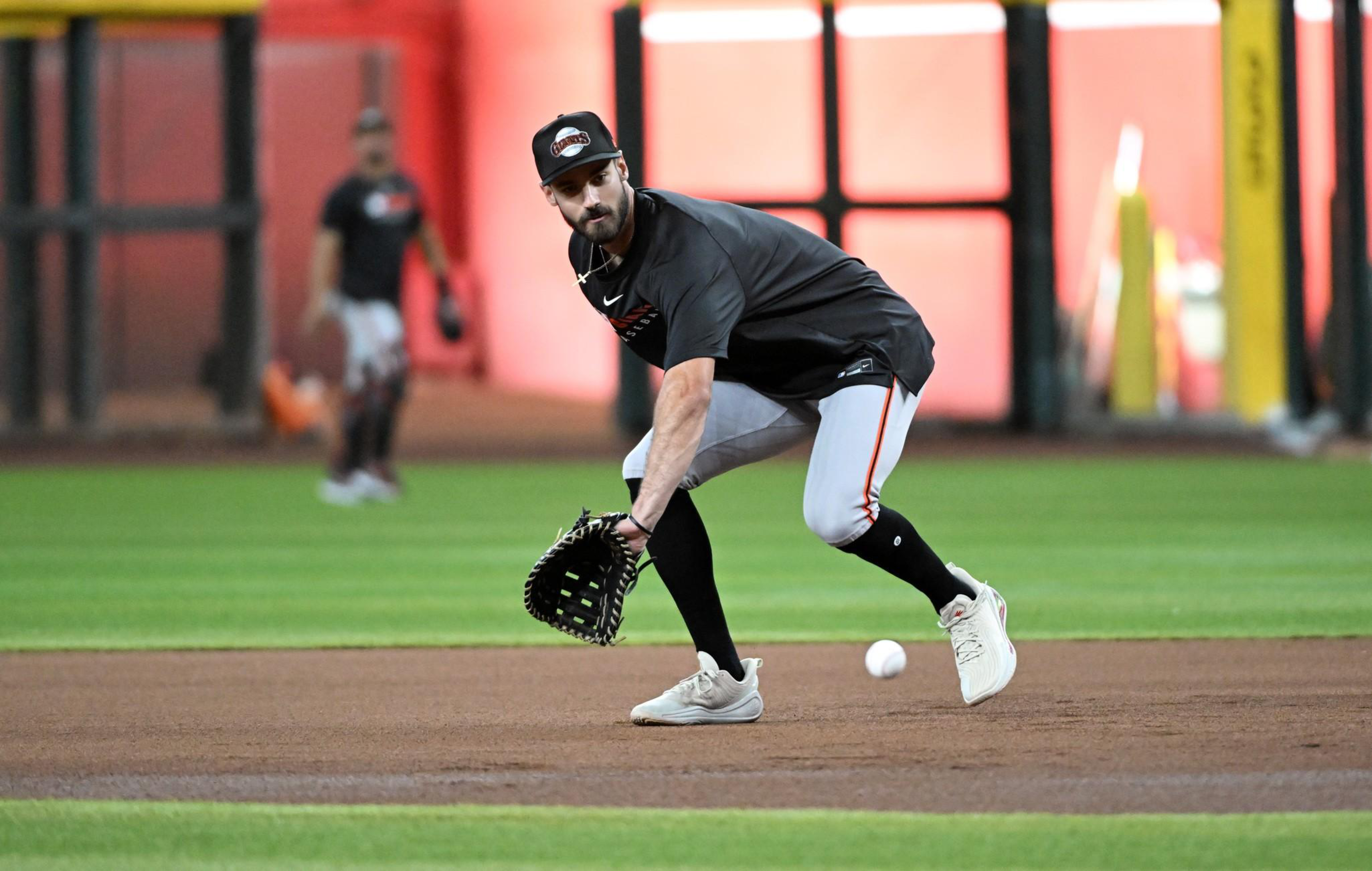 A baseball player wearing a black shirt, gray pants, and a glove is crouching to field a ground ball on a baseball field.
