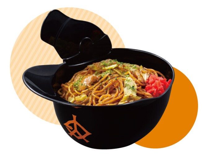 A black plastic baseball helmet filled with light brown cooked noodles with red pickled ginger. 