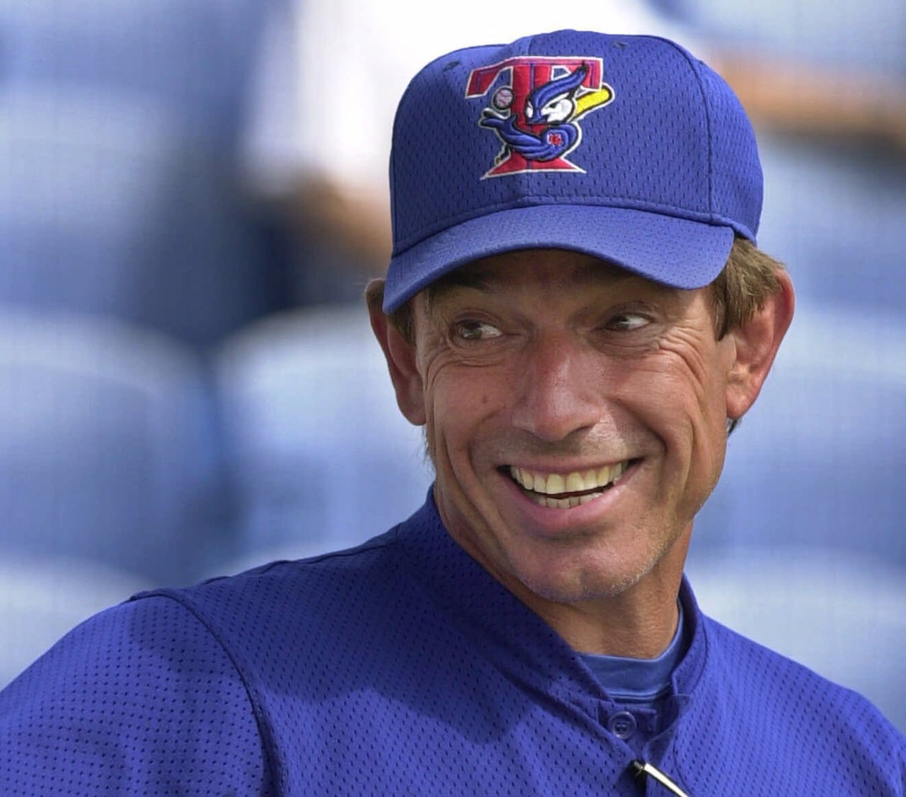 A man in a blue jays baseball hat and shirt smiles and points off camera