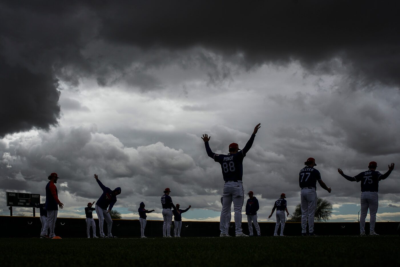 Texas Rangers pitchers stretch under threatening storm clouds during a spring training...