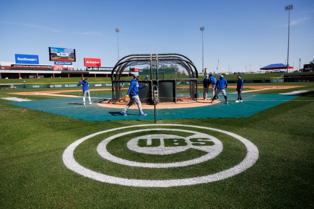 The Cubs logo sits on the field while players attend batting practice during spring training at Sloan Park on Feb. 19, 2026, in Mesa, Ariz. (Armando L. Sanchez/Chicago Tribune)