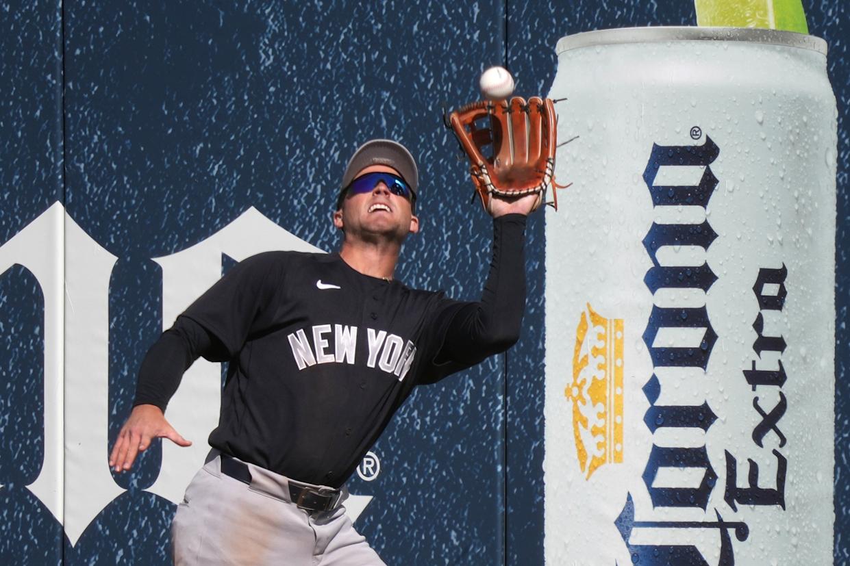 Max Schuemann of the New York Yankees catches a fly ball next to a large advertisement for Corona Extra beer.