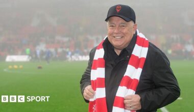 Ron Fowler with a Lincoln City cap and scarf on while stood on the pitch at the LNER Stadium