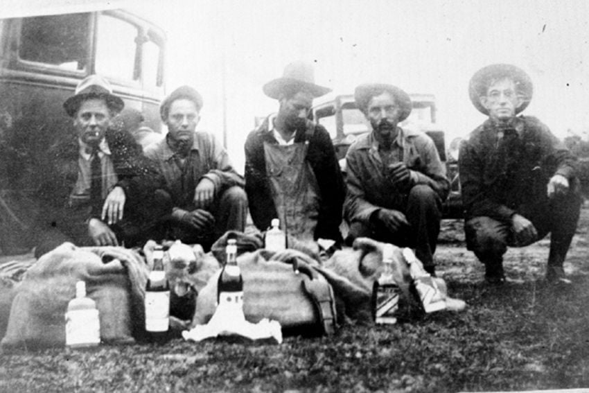 Black and white photos of Mexican tequileros caught on the border in Texas in the 1920s. The three tequileros are posed with two border authorities with the confiscated sacks of alcohol in front of them.