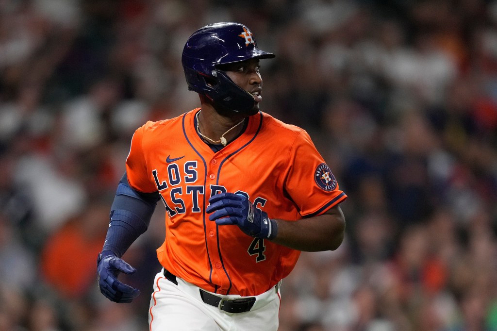 A Houston Astros player in an orange jersey with "Los Astros" and the number 4, wearing a dark blue helmet and gloves, looking to his right during a baseball game.