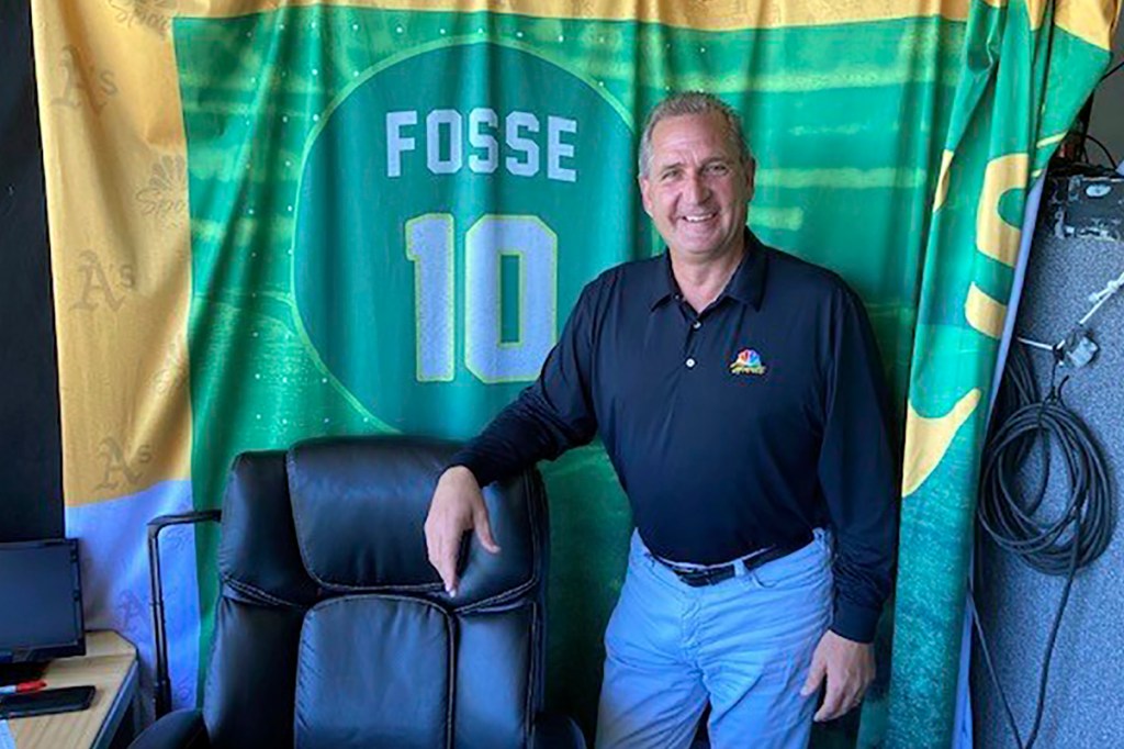 Oakland Athletics broadcaster Glen Kuiper poses next to the Ray Fosse backdrop in the TV booth at the Coliseum before a baseball game against the San Francisco Giants on Aug. 6, 2022, in Oakland, Calif.