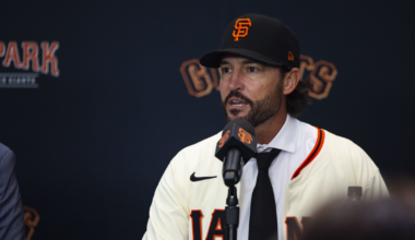 A man wearing a San Francisco Giants baseball jersey and cap speaks into a microphone at a press conference.