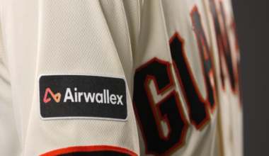 A beige baseball jersey features "GIANTS" in black and orange letters across the chest, with a black and orange trimmed sleeve patch labeled "Airwallex."