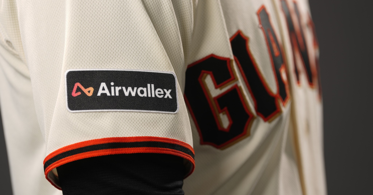 A beige baseball jersey features "GIANTS" in black and orange letters across the chest, with a black and orange trimmed sleeve patch labeled "Airwallex."