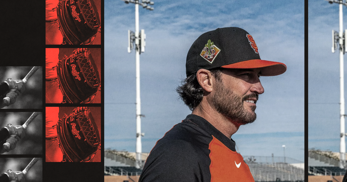A baseball player wearing a black and orange Giants uniform faces right on a field with stadium lights and bleachers behind him.